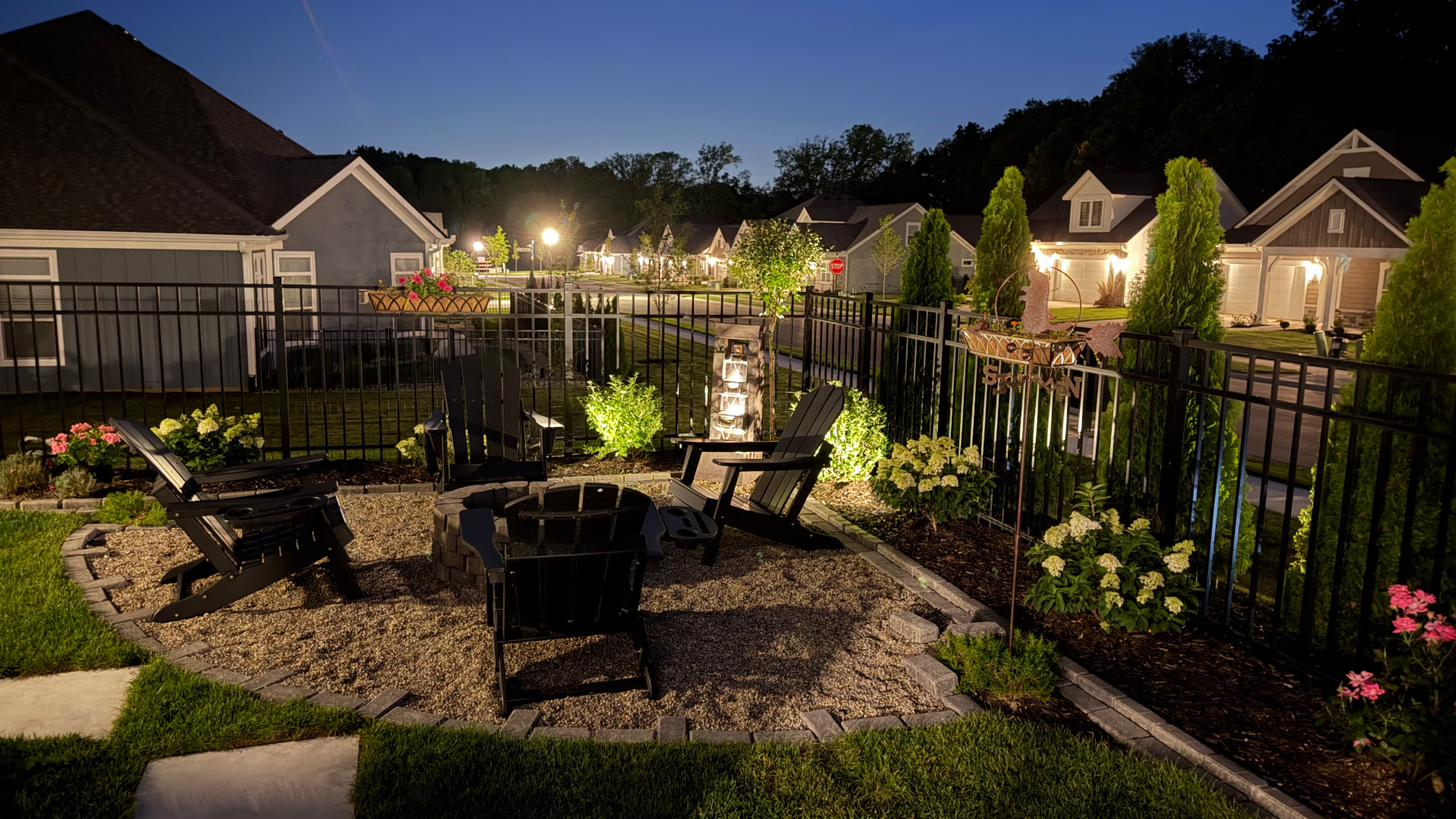Neighborhood fire pit patio lit up at dusk with homes in the background