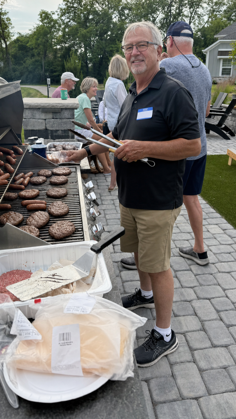 A neighbor grilling burgers and hot dogs at a community cookout